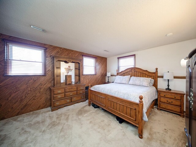 bedroom with wood walls, light colored carpet, and a textured ceiling