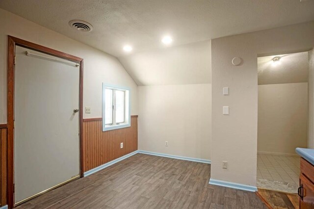 bonus room with a wainscoted wall, vaulted ceiling, wood finished floors, a textured ceiling, and visible vents