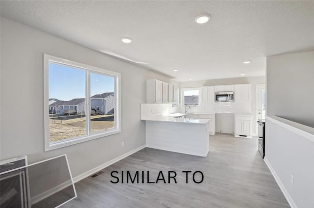 kitchen with white cabinetry, stainless steel microwave, a healthy amount of sunlight, and a peninsula