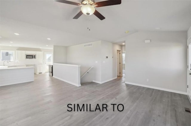 unfurnished living room with vaulted ceiling, baseboards, light wood finished floors, ceiling fan, and visible vents