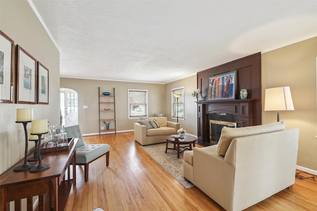 living room with a fireplace with flush hearth, ornamental molding, arched walkways, light wood-type flooring, and baseboards