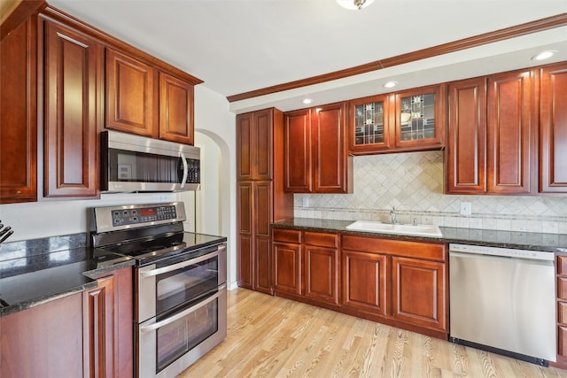 kitchen with light wood finished floors, stainless steel appliances, backsplash, reddish brown cabinets, and a sink