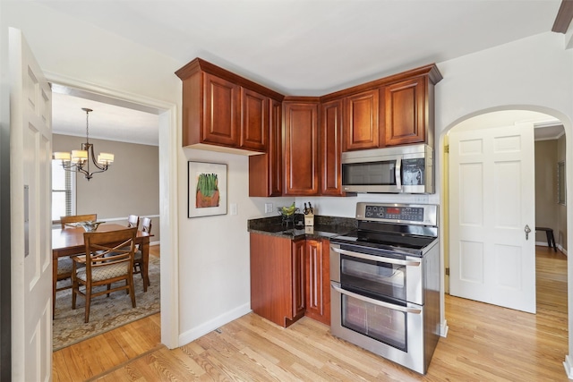 kitchen featuring light wood-style floors, arched walkways, an inviting chandelier, baseboards, and appliances with stainless steel finishes