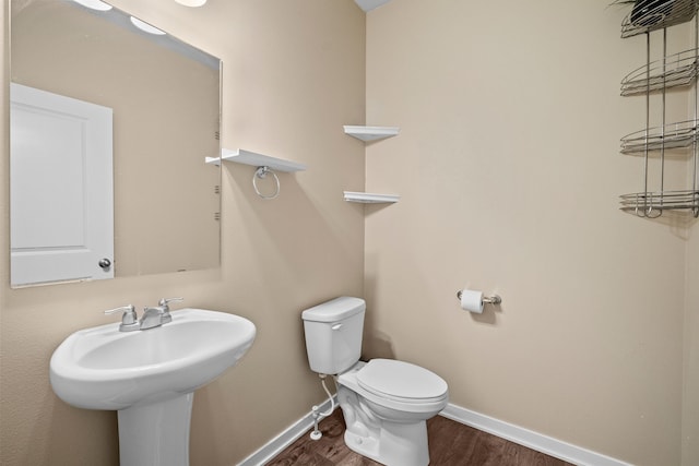 half bath featuring wood finished floors, toilet, baseboards, and a sink