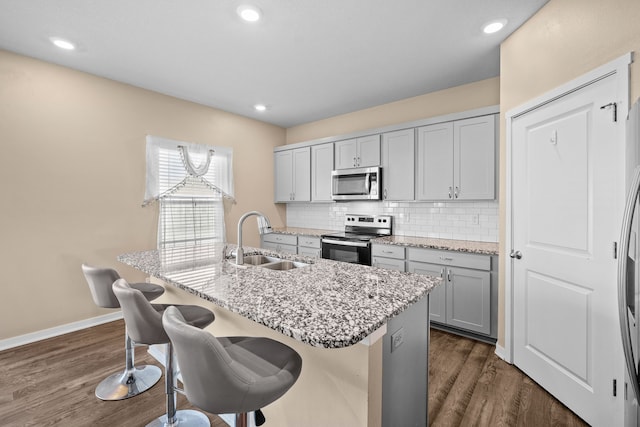 5506 145th St, Urbandale, IA 50323 - kitchen featuring stainless steel appliances, a sink, a kitchen island with sink, tasteful backsplash, and a kitchen bar
