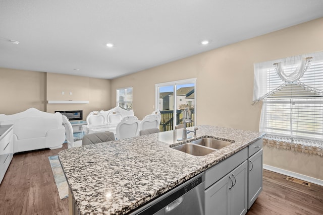 kitchen with stainless steel dishwasher, dark wood-type flooring, a center island with sink, light stone counters, and recessed lighting