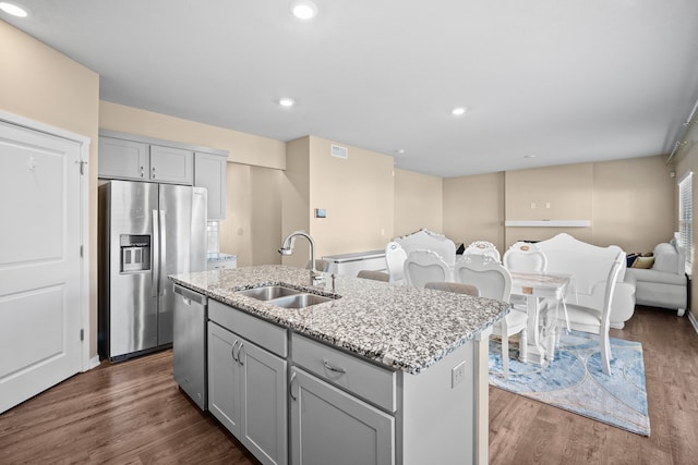 kitchen with stainless steel appliances, a sink, gray cabinetry, open floor plan, and a kitchen island with sink
