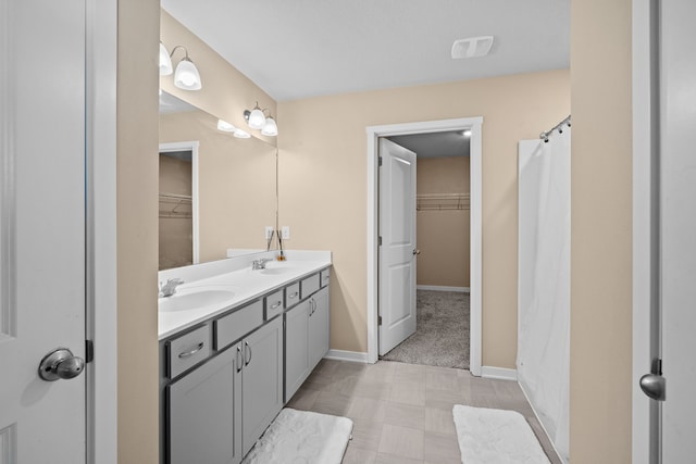 full bath featuring tile patterned floors, a walk in closet, baseboards, and double vanity