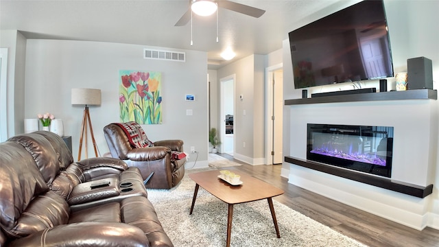 living room with wood finished floors, a ceiling fan, a glass covered fireplace, and baseboards