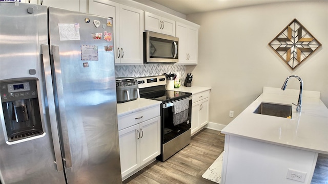 kitchen featuring appliances with stainless steel finishes, a sink, light wood finished floors, tasteful backsplash, and white cabinetry