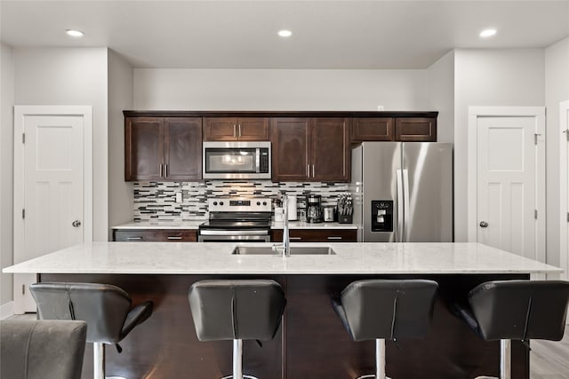 17127 Blue Sage Ln, Urbandale, IA 50323 - kitchen with stainless steel appliances, dark brown cabinetry, a sink, a breakfast bar, and decorative backsplash