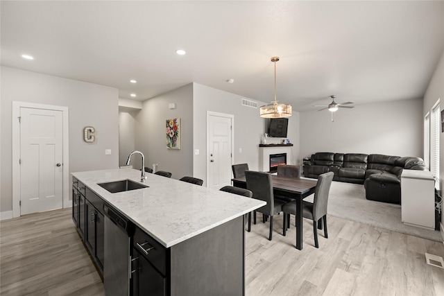 17127 Blue Sage Ln, Urbandale, IA 50323 - kitchen with a sink, a glass covered fireplace, dishwasher, light wood finished floors, and dark cabinets