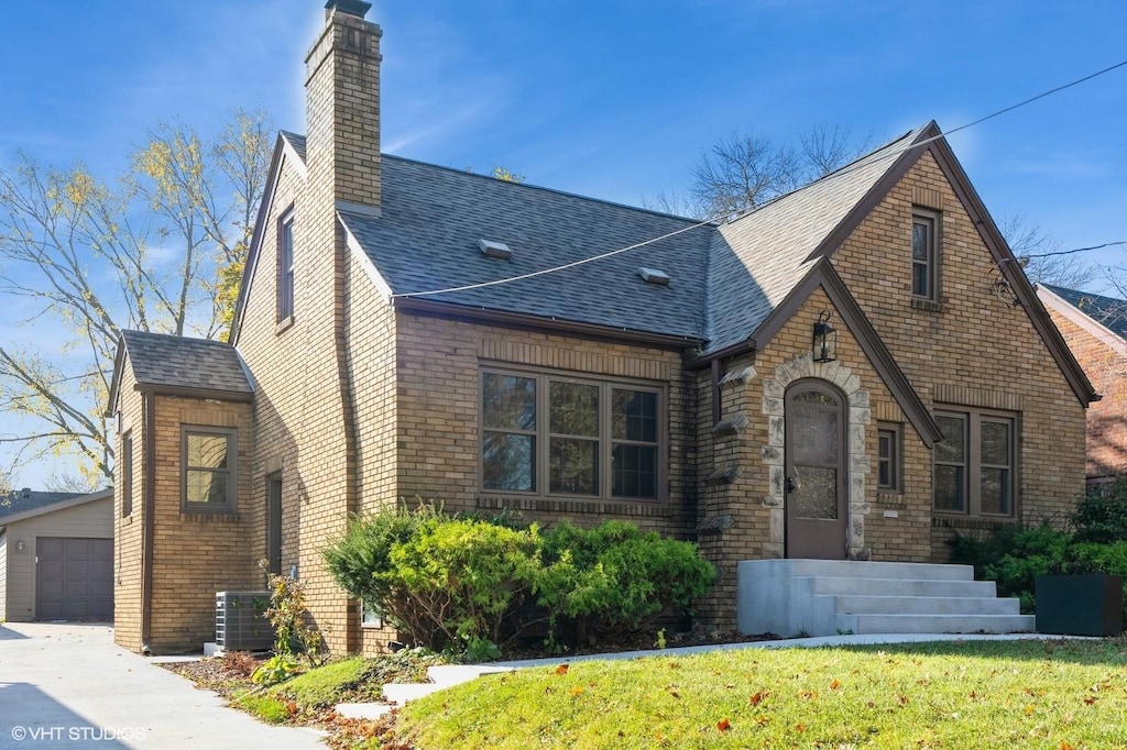 4320 New York Ave, Des Moines, IA 50310 - tudor-style house with central AC unit, a chimney, brick siding, roof with shingles, and an outbuilding