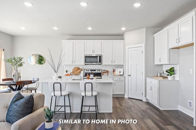 kitchen with appliances with stainless steel finishes, a kitchen island with sink, light countertops, and white cabinetry