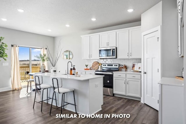 kitchen with dark wood-style floors, backsplash, white cabinets, a breakfast bar area, and stainless steel appliances