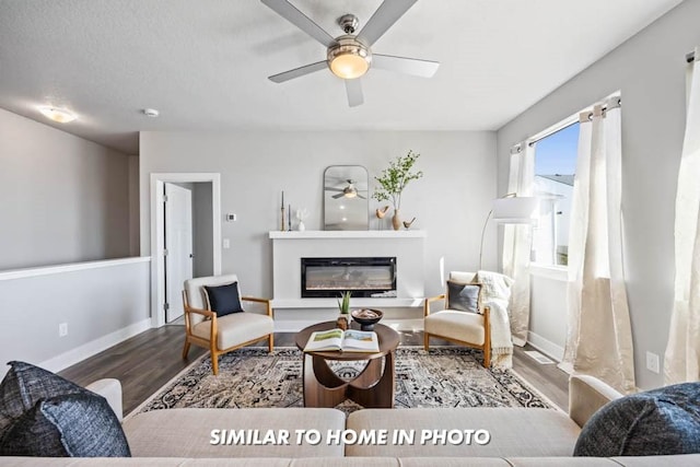 living area with a glass covered fireplace, baseboards, a textured ceiling, ceiling fan, and wood finished floors