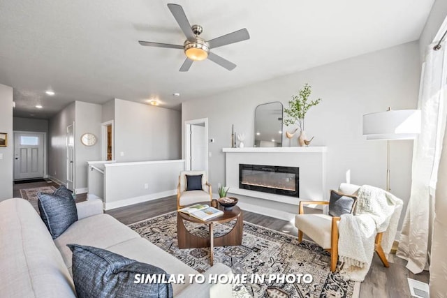 living room featuring a ceiling fan, wood finished floors, baseboards, and a glass covered fireplace