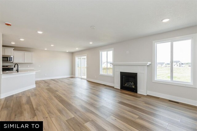 1012 Willow Valley Dr, Norwalk, IA 50211 - unfurnished living room with a glass covered fireplace, visible vents, a healthy amount of sunlight, and light wood-style floors