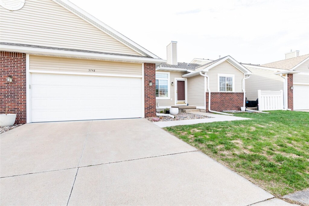 single story home with driveway, a front yard, a chimney, an attached garage, and brick siding