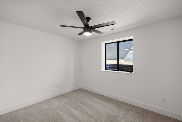 spare room with ceiling fan, a textured ceiling, light colored carpet, visible vents, and baseboards