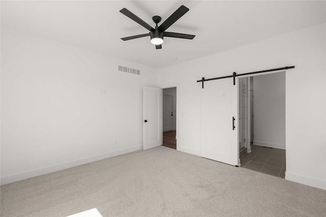 unfurnished bedroom featuring carpet, a ceiling fan, visible vents, a barn door, and baseboards