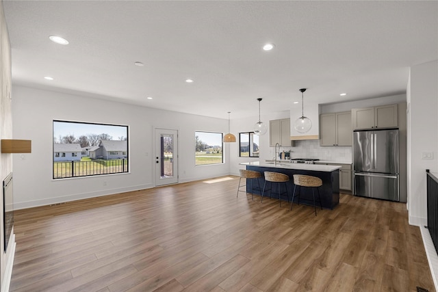 kitchen with light countertops, freestanding refrigerator, a kitchen bar, gray cabinetry, and backsplash