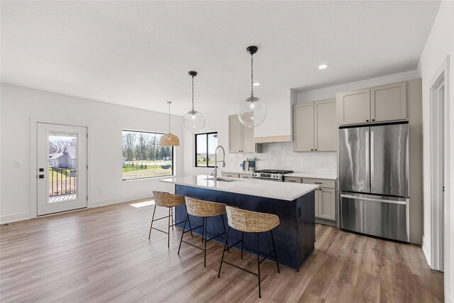 kitchen featuring freestanding refrigerator, gray cabinetry, a center island with sink, stove, and a sink