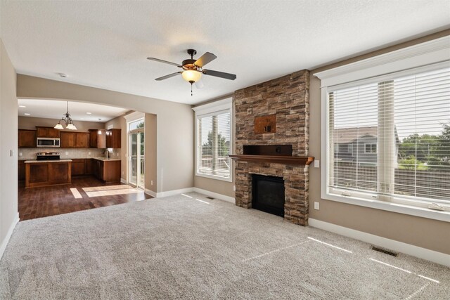 3555 NW 164th St, Clive, IA 50325 - unfurnished living room featuring carpet flooring, a ceiling fan, a stone fireplace, a chandelier, and arched walkways