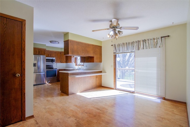 1412 Country Club Dr, Pella, IA 50219 - kitchen featuring stainless steel appliances, a peninsula, brown cabinetry, a ceiling fan, and light countertops