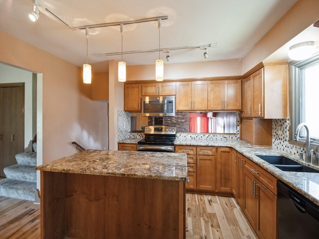 kitchen with a sink, light wood-style floors, light stone countertops, a center island, and appliances with stainless steel finishes