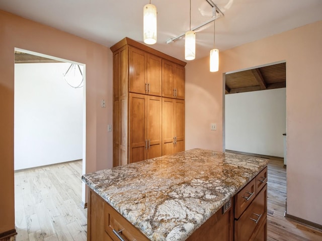 kitchen featuring light wood finished floors, brown cabinetry, and light stone counters