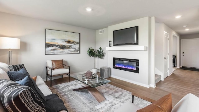 living area featuring a glass covered fireplace, visible vents, recessed lighting, wood finished floors, and baseboards