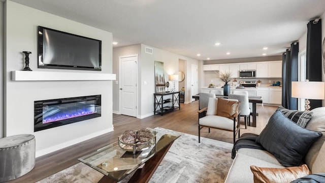 living area featuring a glass covered fireplace, baseboards, recessed lighting, light wood-style floors, and visible vents