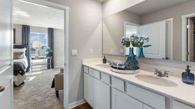 ensuite bathroom with a sink, baseboards, double vanity, and a textured ceiling