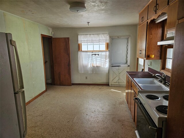 kitchen with baseboards, a sink, freestanding refrigerator, electric stove, and brown cabinets