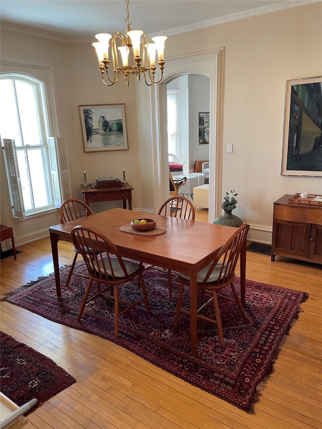 dining room featuring arched walkways, a notable chandelier, ornamental molding, and light wood-style floors