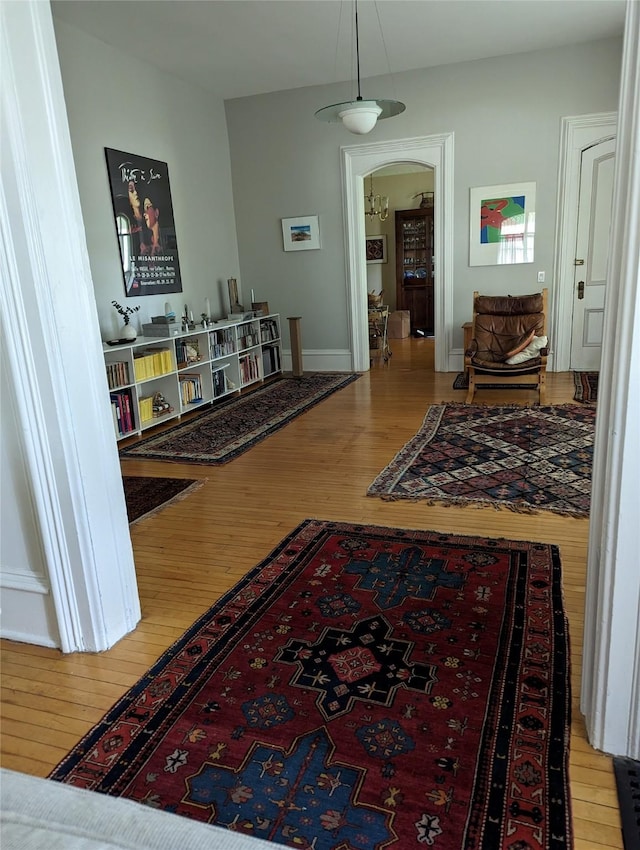 corridor with arched walkways, baseboards, and wood finished floors