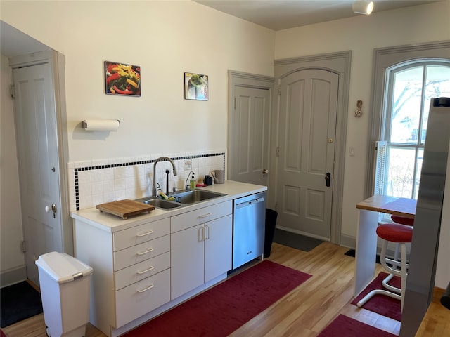 bar featuring a sink, decorative backsplash, light wood-style flooring, and dishwasher