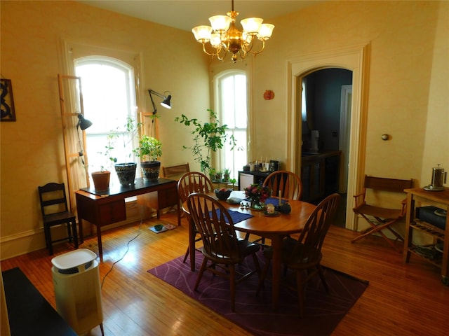 dining room with plenty of natural light, arched walkways, wood finished floors, and a chandelier