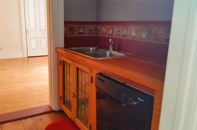 kitchen featuring black dishwasher, baseboards, a sink, and light wood-style floors