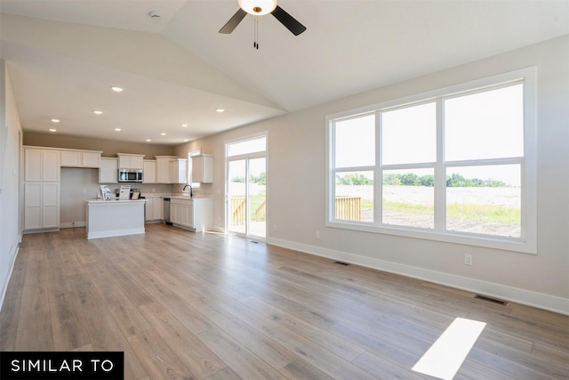 unfurnished living room featuring visible vents, baseboards, a sink, light wood-style flooring, and lofted ceiling