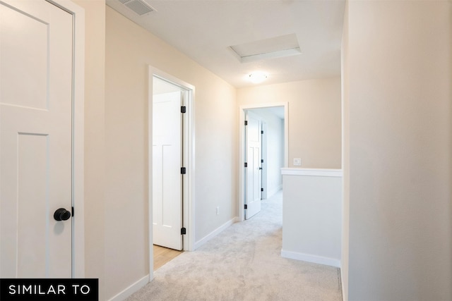 corridor with light carpet, visible vents, baseboards, and attic access