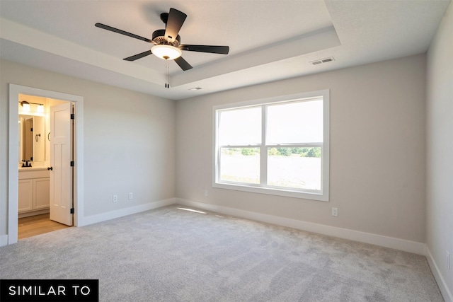 unfurnished bedroom featuring baseboards, visible vents, a tray ceiling, and light colored carpet