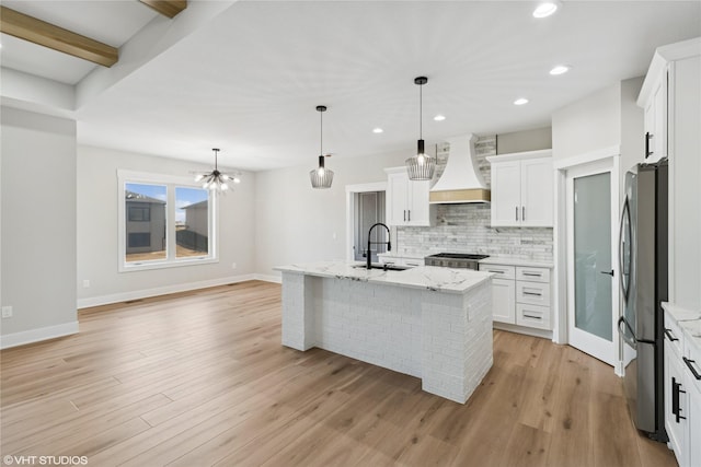 kitchen with light wood-style floors, tasteful backsplash, appliances with stainless steel finishes, a sink, and premium range hood