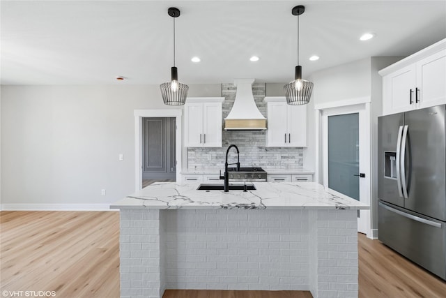 kitchen featuring decorative backsplash, custom range hood, a sink, stainless steel fridge, and light wood finished floors