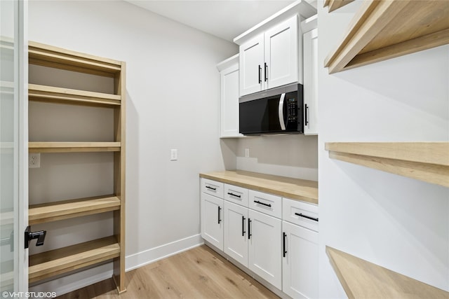 kitchen featuring butcher block counters, light wood-style flooring, white cabinetry, and baseboards