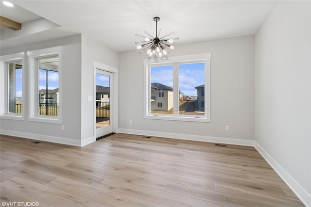 unfurnished dining area with plenty of natural light, light wood finished floors, a notable chandelier, and baseboards