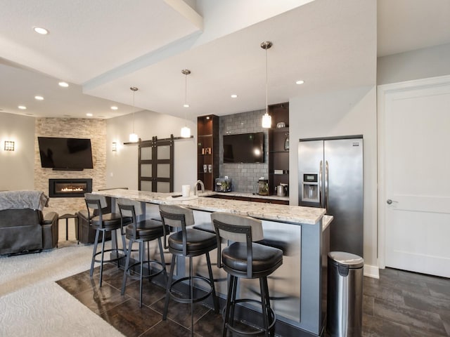 bar with tasteful backsplash, stainless steel fridge, a barn door, a stone fireplace, and recessed lighting