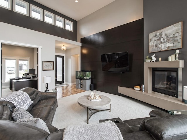 living room featuring baseboards, light wood finished floors, a high ceiling, and a glass covered fireplace