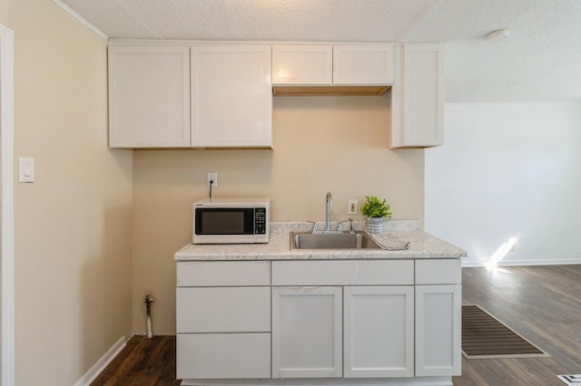 kitchen featuring white microwave, dark wood finished floors, white cabinets, a sink, and baseboards